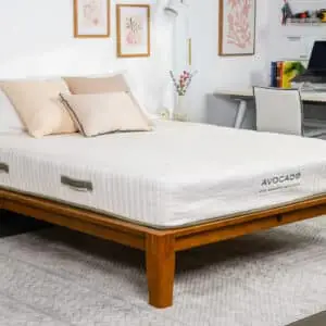 Avocado Eco Organic Mattress on a wooden bed frame with decorative pillows in a modern bedroom setting, showcasing sleep comfort and eco-friendly design.