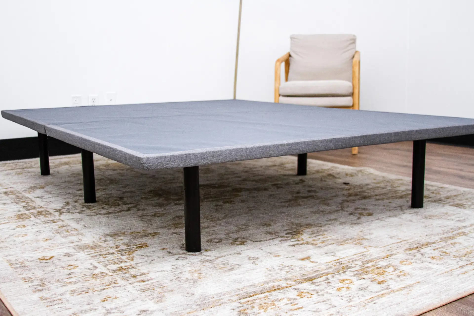 Bedtech X-Plat 4 BedTech X-Plat platform bed frame with a sleek design, featuring a gray fabric surface and sturdy black legs, set on a decorative rug in a modern room.