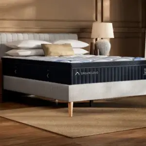 DreamCloud Premier Hybrid mattress on a stylish bed frame with decorative pillows and a bedside lamp, showcasing a modern bedroom setting.