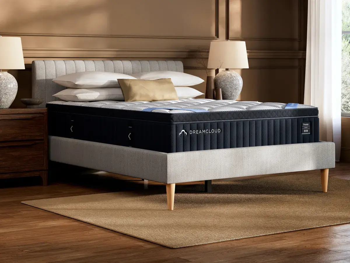 DreamCloud Premier Hybrid mattress on a stylish bed frame in a cozy bedroom setting, featuring soft pillows and a decorative lamp, showcasing premium sleep solutions for better rest.