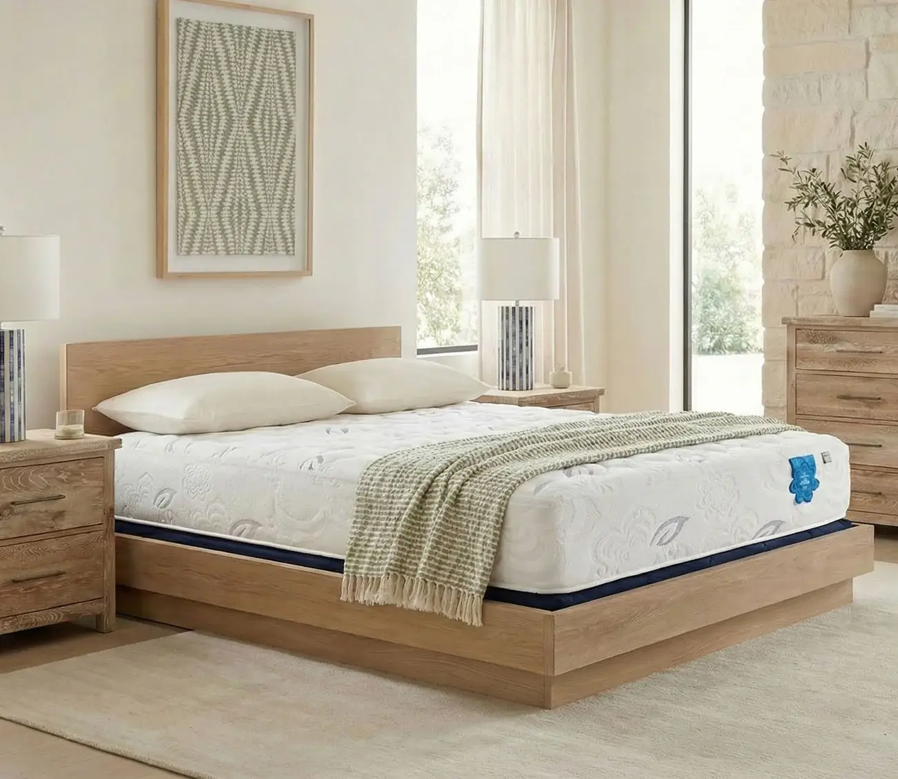 PranaSleep Asha Luxe mattress displayed on a wooden bed frame in a bright, modern bedroom setting, featuring decorative pillows, a cozy throw blanket, and bedside tables with lamps, emphasizing comfort and wellness for a restful sleep experience.