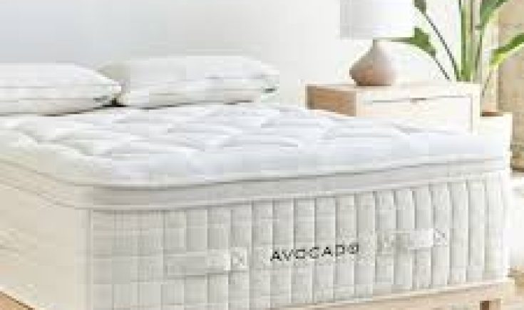 Avocado organic mattress with luxury pillow top, featuring a white tufted design, placed on a wooden bed frame beside a nightstand and lamp, highlighting handcrafted comfort and sustainable materials.