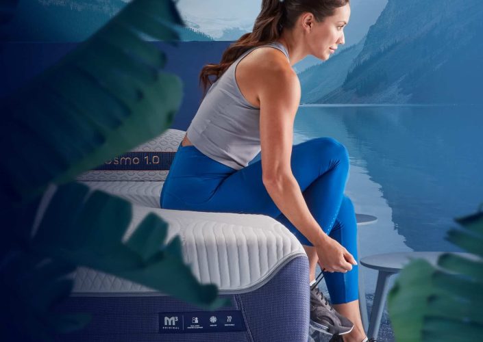 Woman in athletic wear sitting on BedGear M3 mattress, preparing for exercise, with a serene lake and mountains in the background, emphasizing comfort and performance for better sleep and active lifestyle.