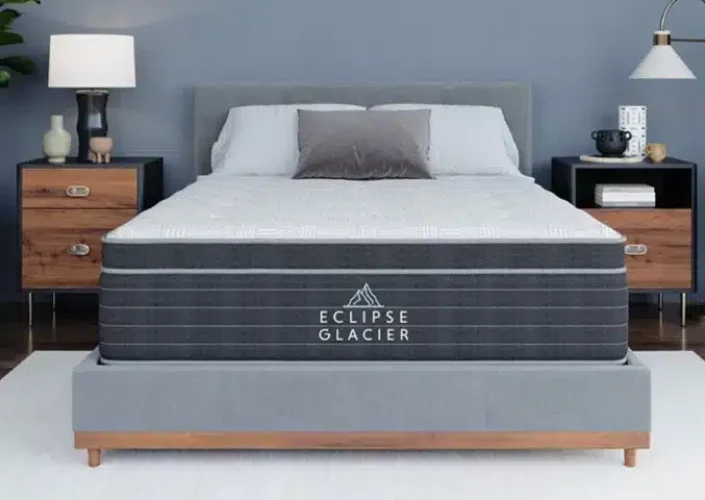 Eclipse Glacier mattress displayed on a modern bed frame, featuring a gray color scheme with decorative pillows, bedside tables, and a stylish lamp, highlighting its hybrid design and comfort features.