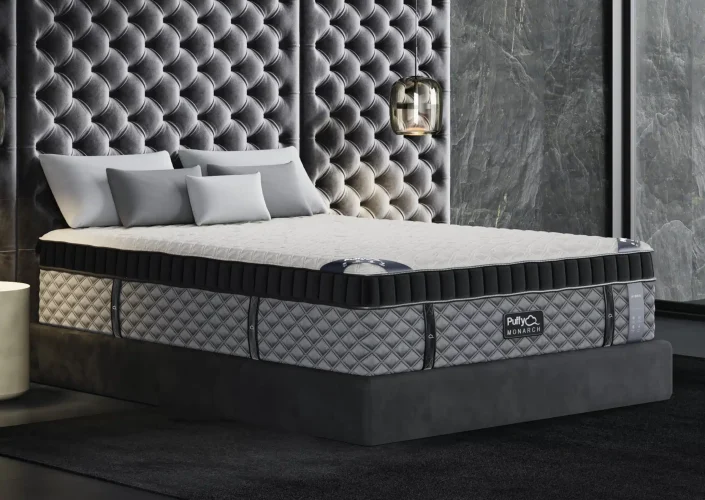 Puffy Monarch Hybrid Mattress displayed in a luxurious bedroom setting with plush upholstered walls, featuring a cooling comfort design and elegant gray color scheme.