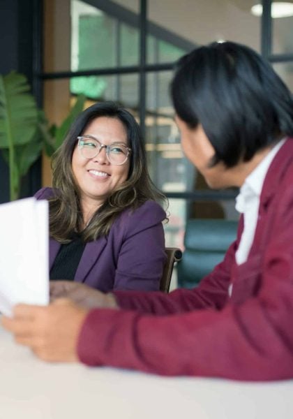Smiling woman in a purple blazer engaging in conversation with a man, discussing health-conscious mattress options at Healthy ZZZ's Sit & Sleep.